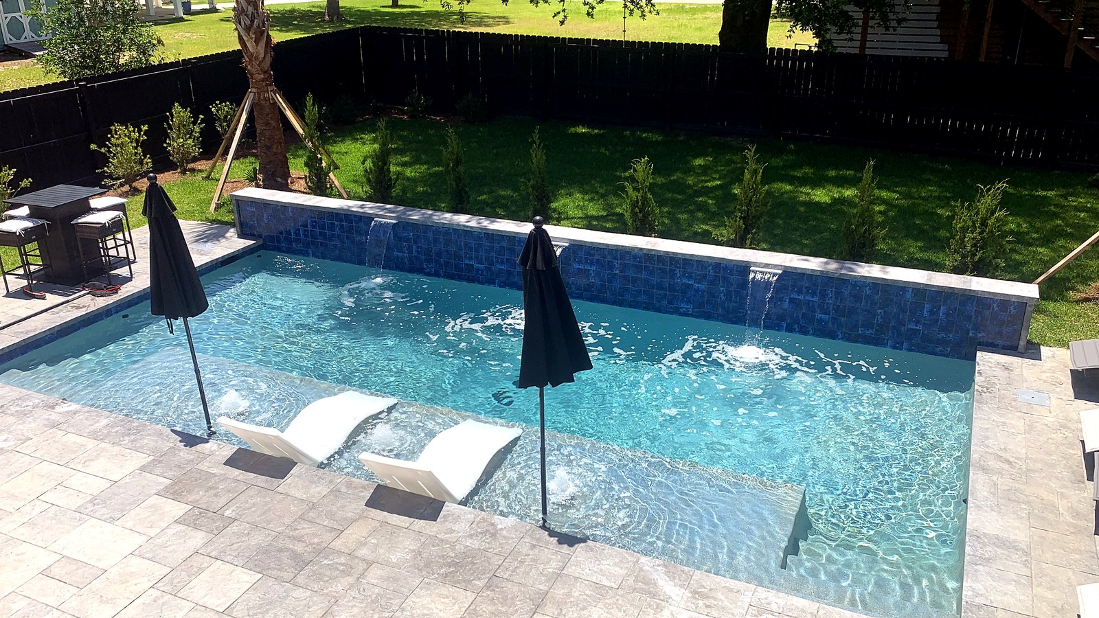 Pool with a raised blue-tile wall, sheer-descent waterfalls and ledge loungers at a custom pool in Pass Christian