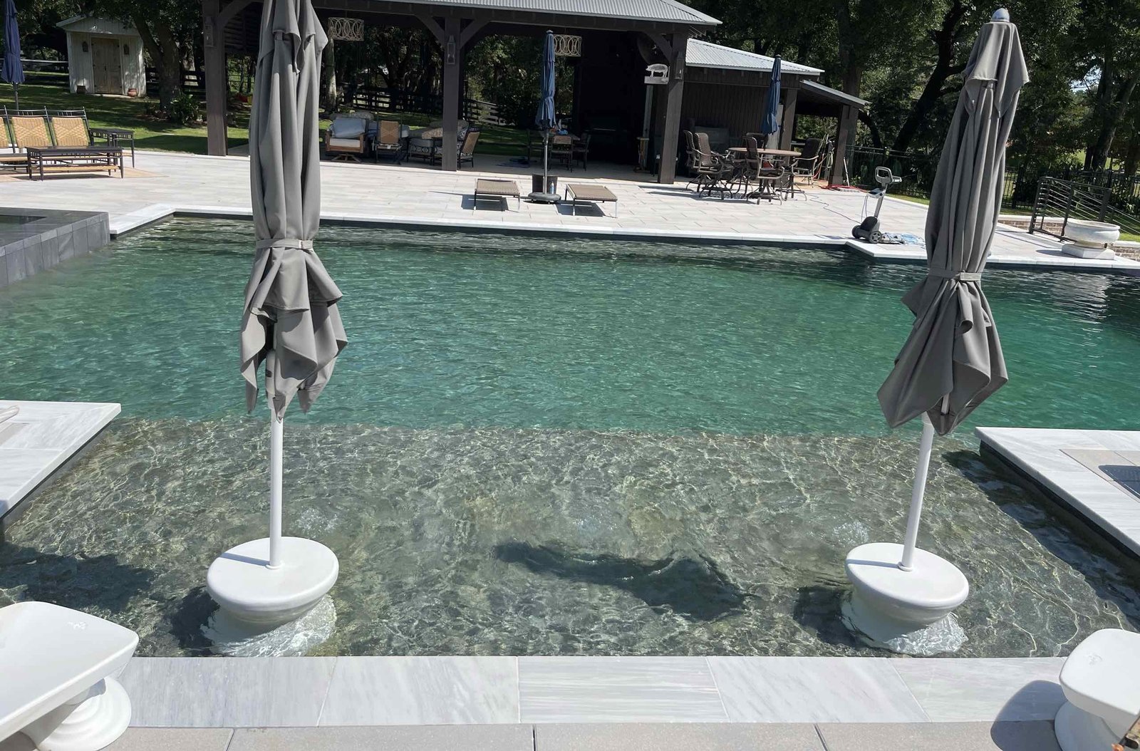 Tanning ledge with in-water umbrellas at a custom pool in Pass Christian