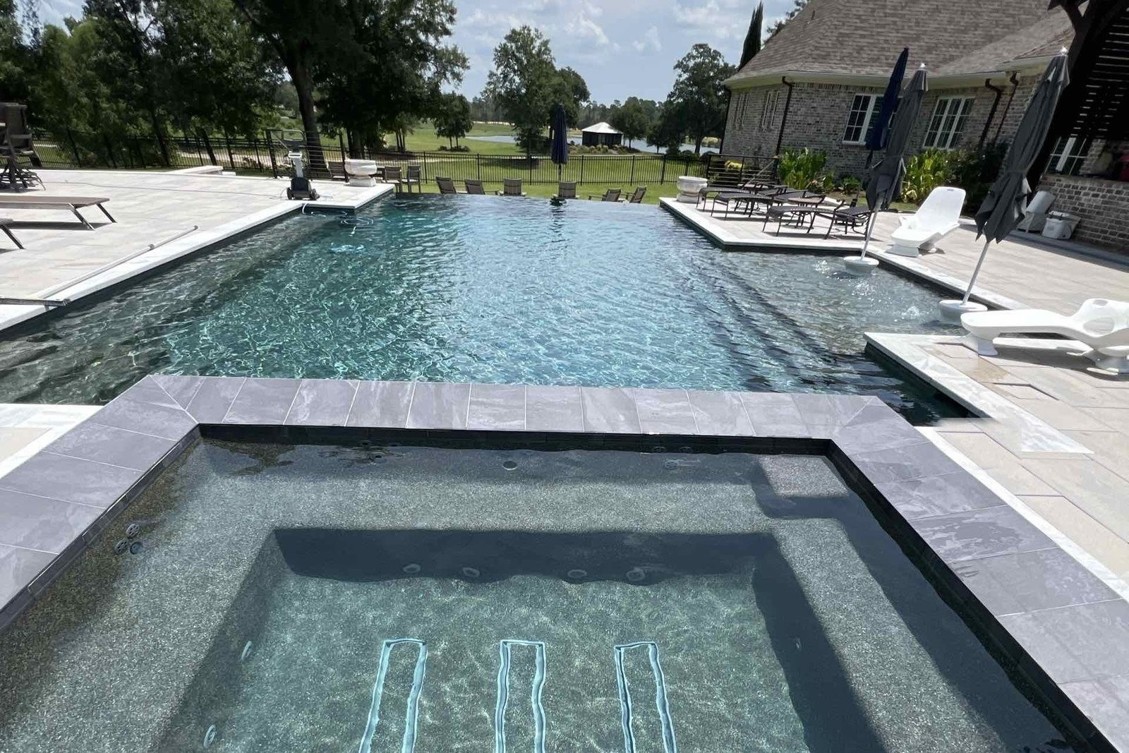 Spa in front of an infinity-edge pool looking out over a lake at a custom pool in Pass Christian
