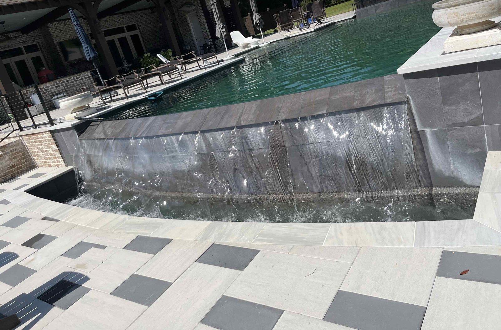 Spa spillover sheeting into a custom pool with slate tile and a paver deck in Pass Christian