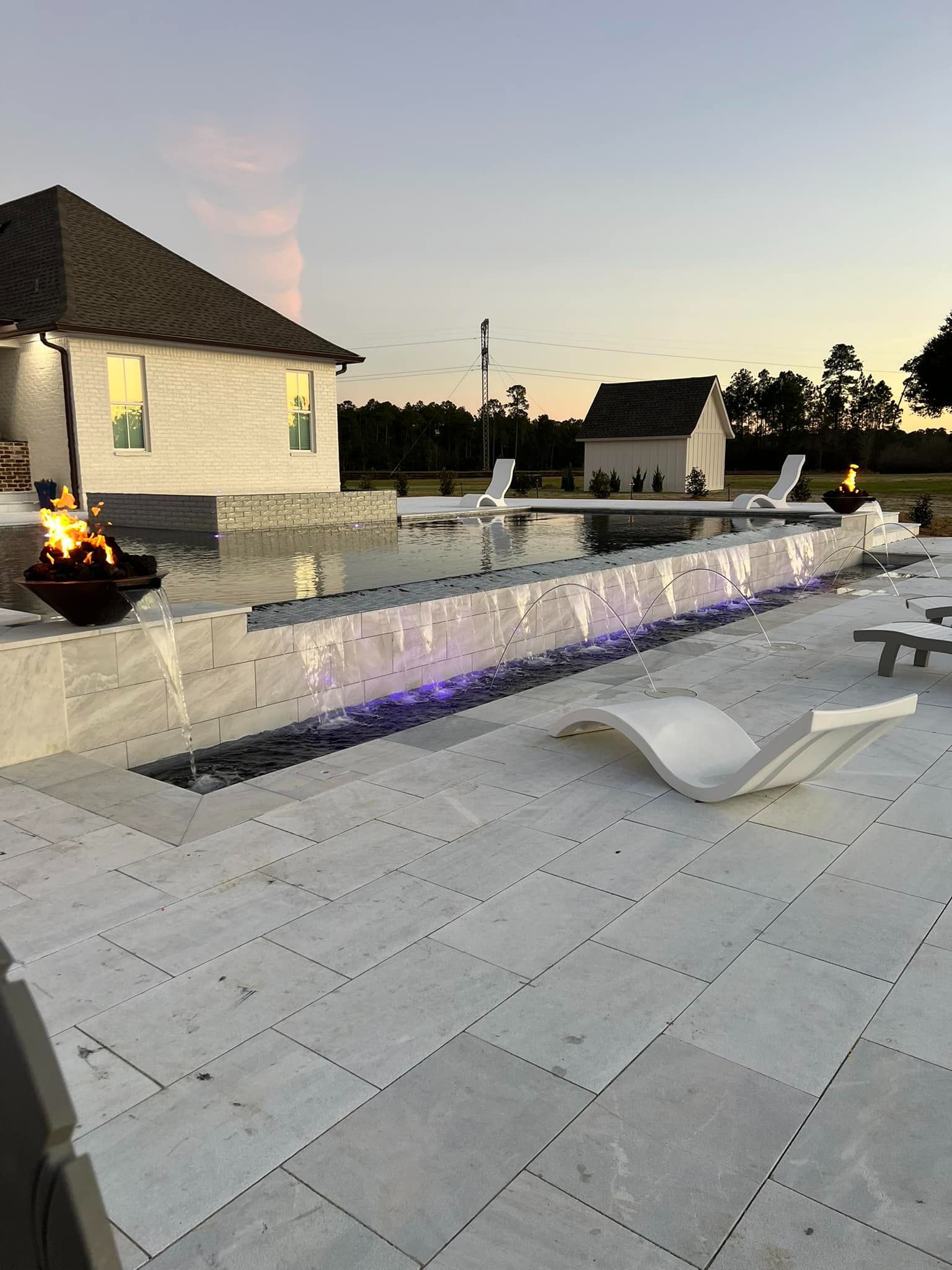 New pool at dusk with a fire bowl, sheer descent and paver deck